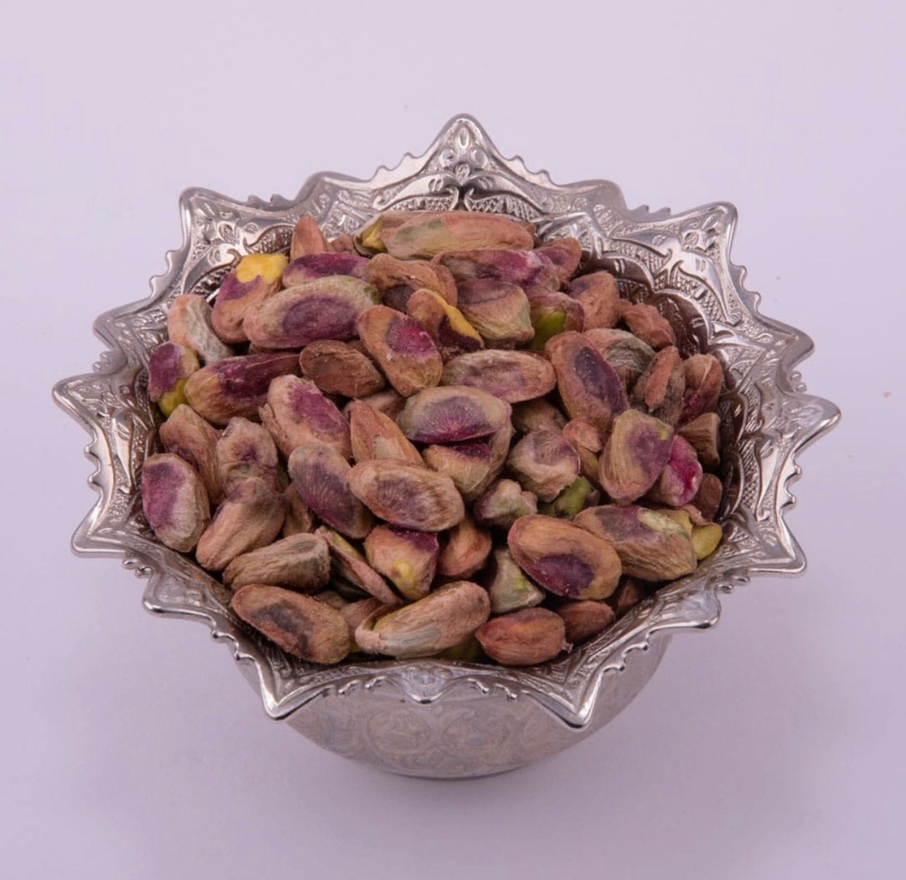 Pistachios in a decorative silver bowl on a white background