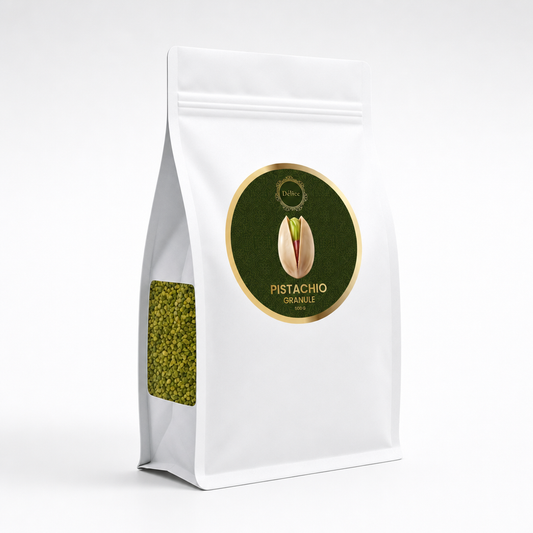 A white stand-up pouch of pistachio granules with a circular green and gold label on the front and a clear window showing green pistachio pieces inside, photographed on a light gray background.