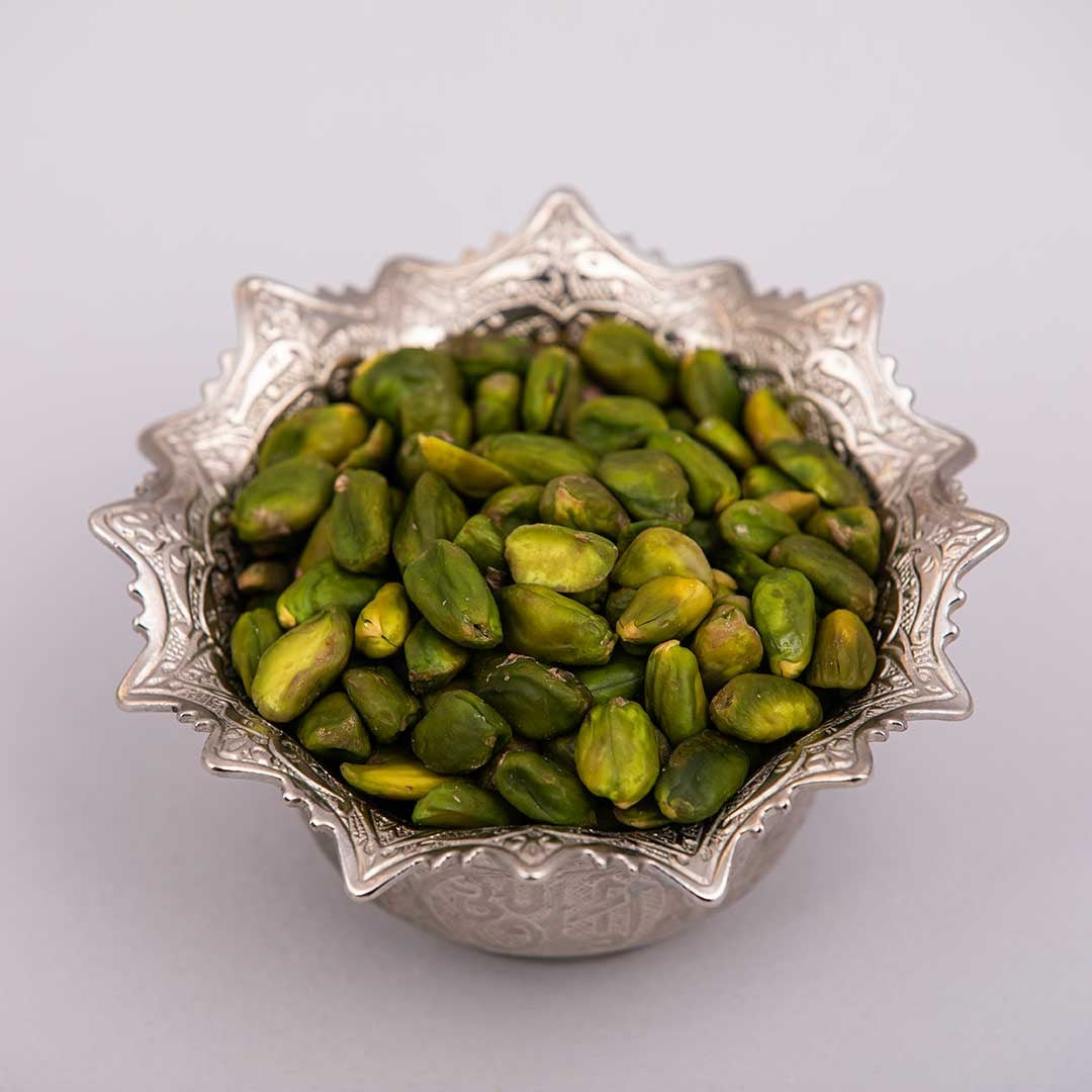 Fresh and premium green peeled pistachios kernels on a silver bowl.