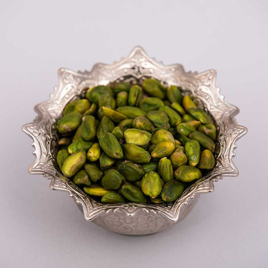 Fresh and premium green peeled pistachios kernels on a silver bowl.
