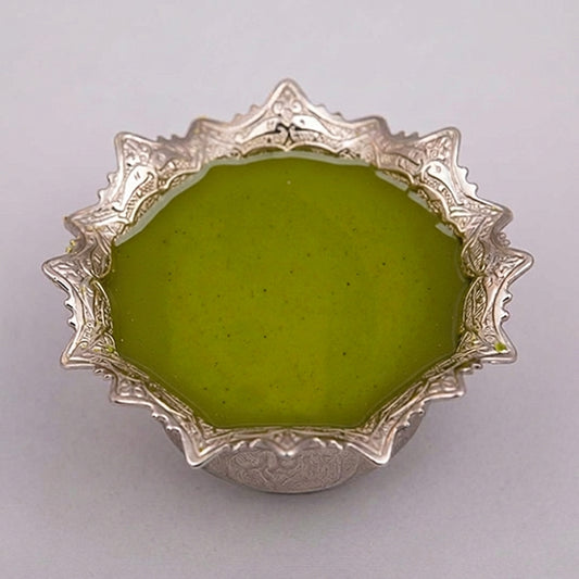 A small ornate silver bowl filled with premium Iranian pistachio paste, photographed from above on a plain light background.